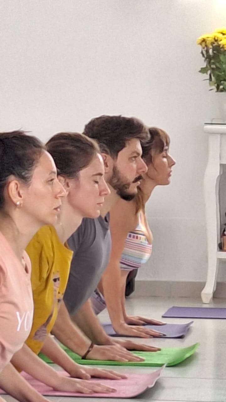 Alunos em aula prática de Yoga sobre colchonetes coloridos no salão do ashram