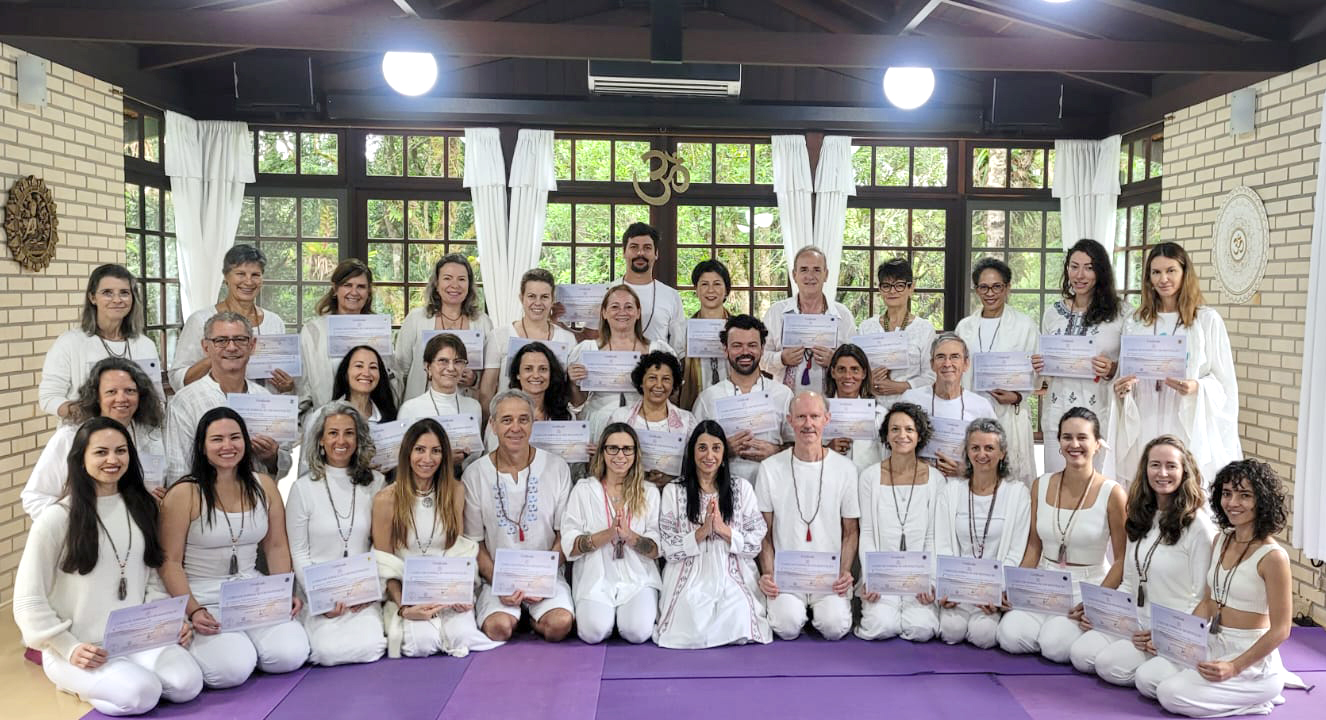 Formandos segurando certificados em sala com janelas amplas e Om dourado ao fundo