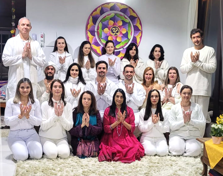 Turma de formandos em posição de Namaste em frente a um mandala colorido com Om