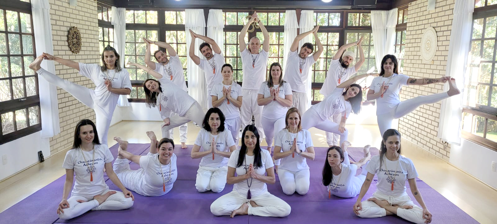 Formandos em poses de yoga no salão do ashram com colchonetes lilases