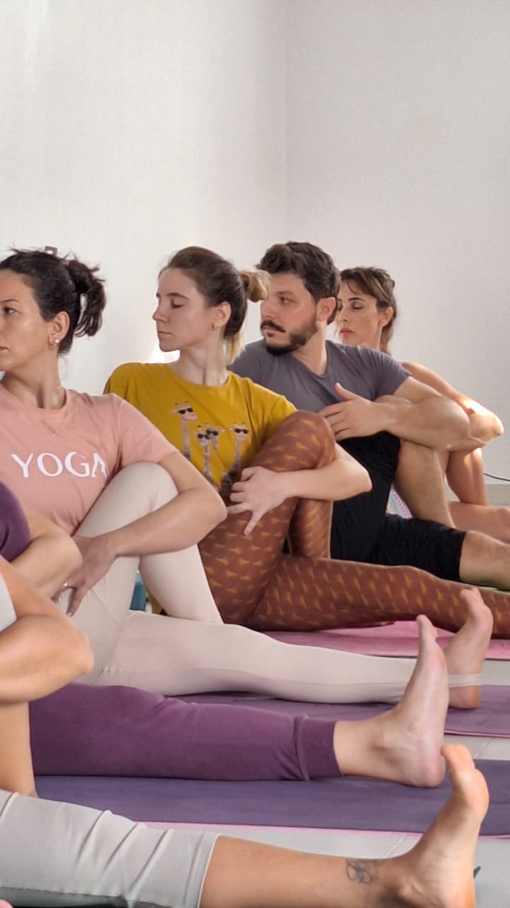 Alunos em aula prática de Yoga realizando alongamento sentado no salão do ashram